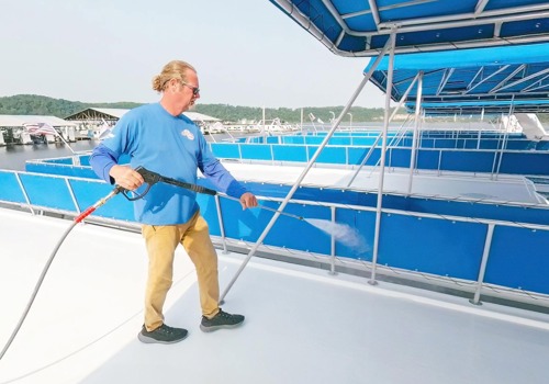 A marina worker uses a pressure washer to clean the deck of a pontoon on a sunny day.